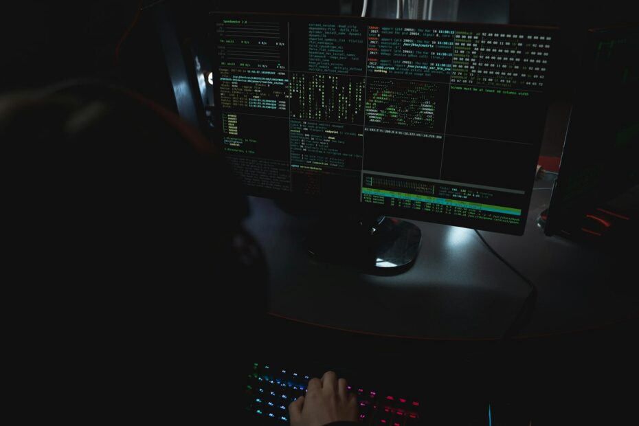 Dark room setup with code displayed on PC monitors highlighting cybersecurity themes.