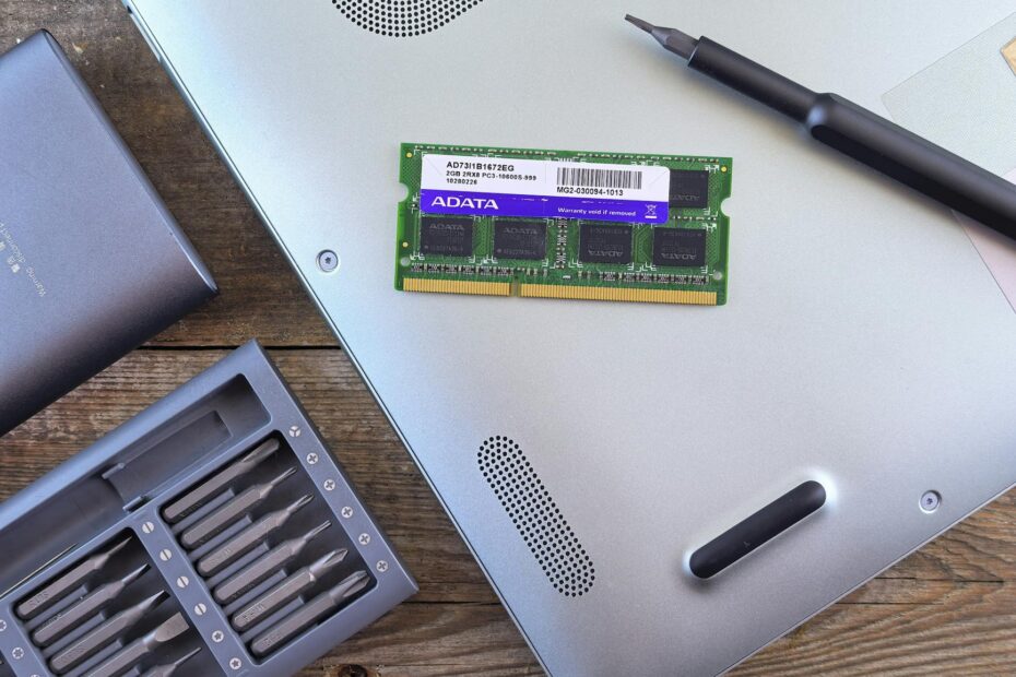 Close-up of an open laptop with RAM module, screwdriver, and toolset on a wooden
