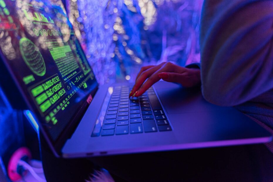 Close-up of hands typing on a laptop displaying cybersecurity graphics, illumina