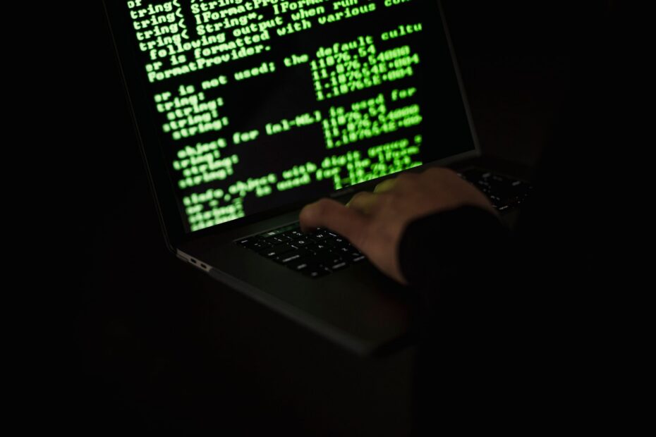 Crop unrecognizable computer geek typing on netbook with codes on screen while hacking system in dar